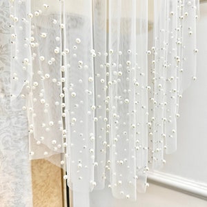 May include: White tulle fabric with pearl embellishments. The fabric is draped and the pearls are scattered throughout the fabric.