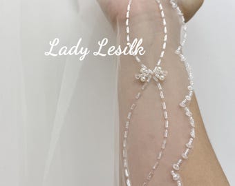 May include: A sheer white bridal veil with delicate beaded embellishments. The veil features a floral design with small pearls and rectangular beads. The text "Lady Lesilk" is visible on the veil.