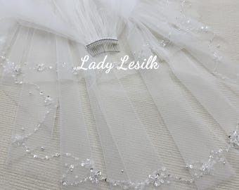 May include: A white bridal veil with a comb, decorated with sparkling beads and floral details along the edge. The veil is made of sheer fabric and features the text "Lady Lesilk".