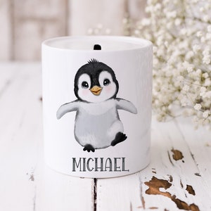 May include: White ceramic money box featuring a cartoon penguin illustration and the name "MICHAEL" printed below.