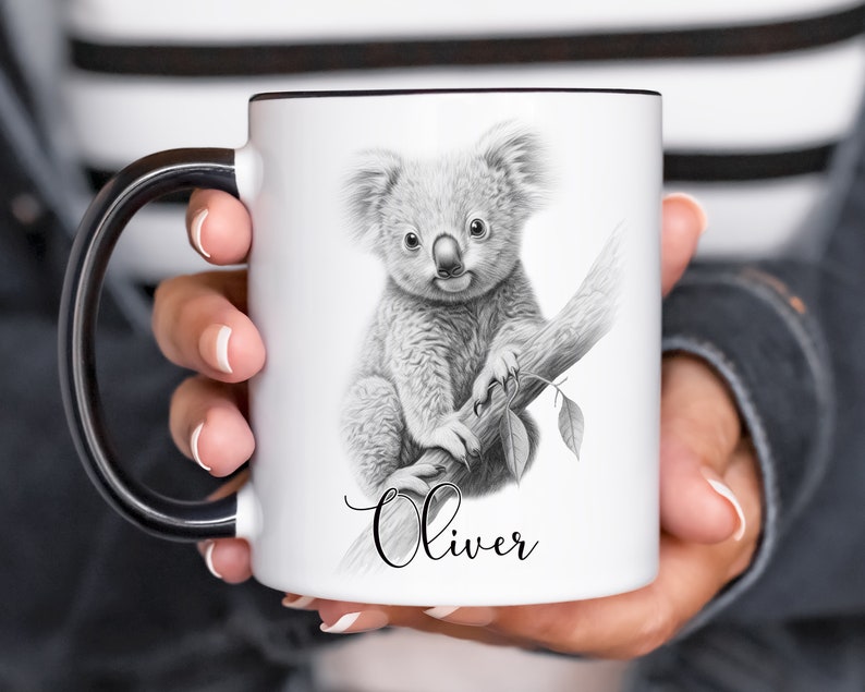 May include: White ceramic mug with a black handle. The mug features a black and white pencil drawing of a koala bear sitting on a branch. The name "Oliver" is written in cursive below the koala.