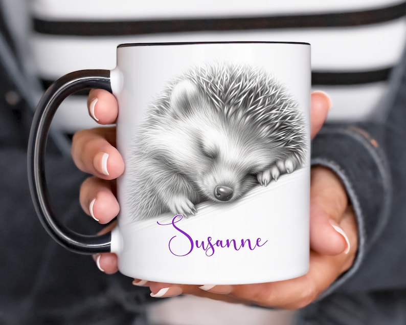 May include: White ceramic mug with a black handle. The mug features a black and white illustration of a sleeping hedgehog. The text "Susanne" is printed in purple below the hedgehog.