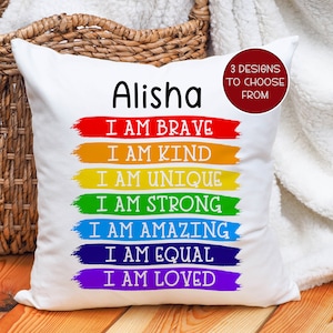 May include: White pillow with the name "Alisha" printed on it. The pillow has a rainbow design with the words "I am brave, I am kind, I am unique, I am strong, I am amazing, I am equal, I am loved" printed on it.