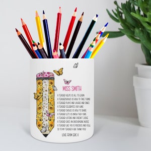 May include: White ceramic pencil holder with a colorful pencil design and the text "Miss Smith" and a poem about teachers. The poem reads: "A teacher helps us all to learn, A teacher shows us how to take turns, A teacher plays and laughs and sings, A teacher celebrates our wins, A teacher shows us how to share, A teacher lets us know they care, A teacher listens and doesn't judge, A teacher gives an encouraging nudge, A teacher like you is precious and full, So to my teacher a big thank you, Love from Eric X."