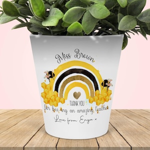 Peut inclure: Pot en céramique blanche avec un motif arc-en-ciel, abeille et nid d'abeilles. Le texte "Miss Brown" est en haut, et le texte "Merci d'être une enseignante extraordinaire Amour d'Enya" est en bas.