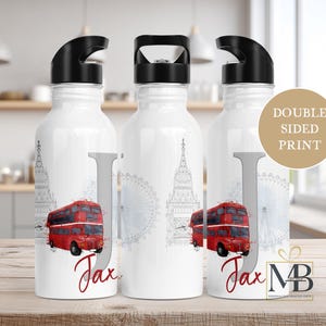 May include: Three white metal water bottles with black lids featuring a London theme. The design includes a red double-decker bus, a grey sketch of Big Ben and the London Eye, a large grey letter J, and the name Jax in red script text.