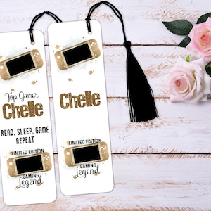 May include: Two white bookmark designs with a gold glitter effect. The top bookmark features a gold Nintendo Switch console with the text "Top Gamer Chelle" and "Read, Sleep, Game Repeat". The bottom bookmark features a gold Nintendo Switch console with the text "Chelle" and "Limited Edition Gaming Legend".