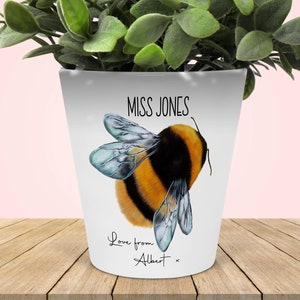 May include: White ceramic planter featuring a bumble bee design. The planter is inscribed with the text "MISS JONES" and "Love from Albert".