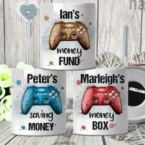 May include: Three white ceramic piggy banks with a watercolor design of a video game controller. The piggy banks are personalized with the names "Ian's", "Peter's", and "Marleigh's". The text on the piggy banks reads "money fund", "saving money", and "money box".