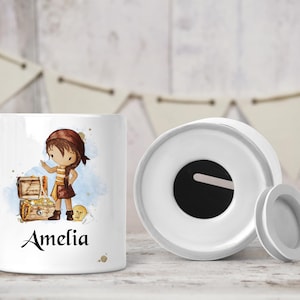 May include: White ceramic money box with a slot on the top. The box features a watercolour illustration of a girl pirate holding a treasure chest. The name Amelia is written below the illustration.