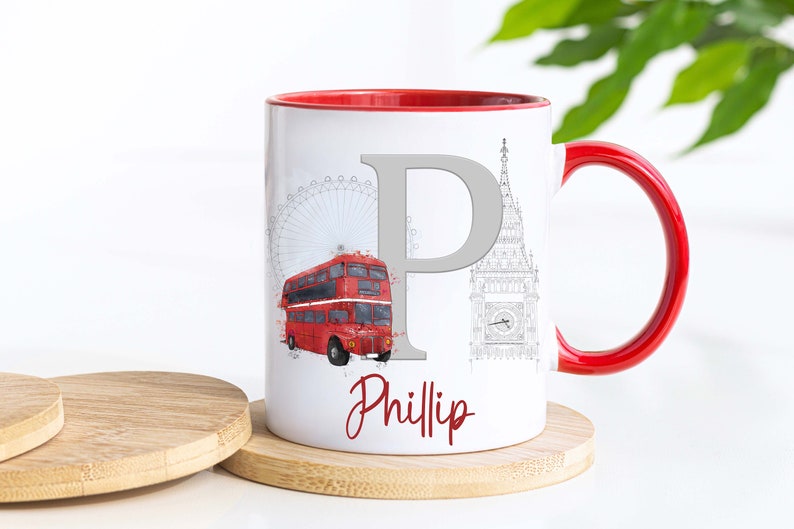 May include: A white ceramic mug with a red interior and handle, featuring a large grey letter P, a red double-decker bus, and a grey line drawing of the London Eye and Big Ben. The name Phillip is printed in red script at the bottom.