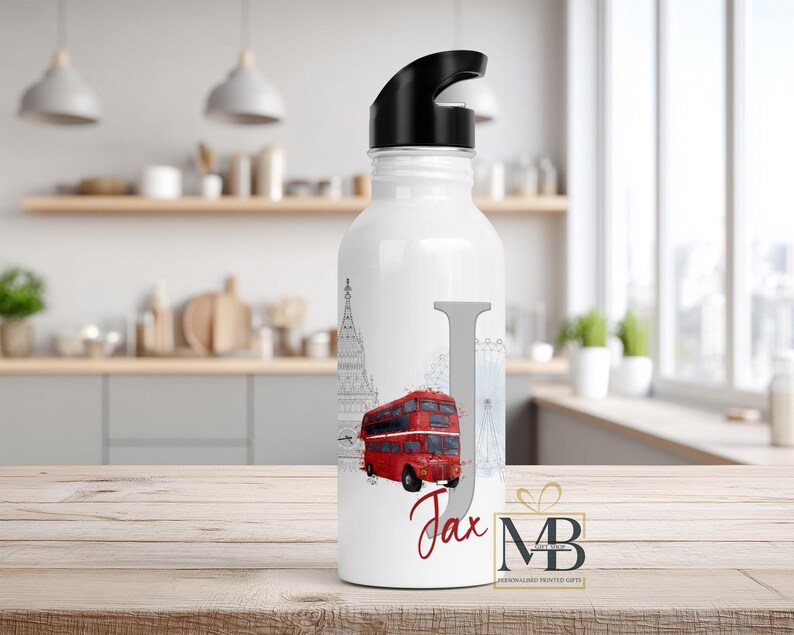 May include: A white water bottle with a black lid featuring a large grey letter J, a red double-decker bus illustration, and the name Jax written in red script. The design includes faint grey outlines of London landmarks like Big Ben.