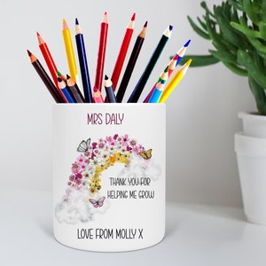 May include: White ceramic pencil holder with a rainbow made of flowers and butterflies. The text "MRS DALY" is at the top, followed by "THANK YOU FOR HELPING ME GROW" and "LOVE FROM MOLLY X".