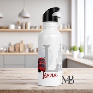 May include: A white water bottle with a black lid featuring a large gray letter L, a red double-decker bus, a gray Ferris wheel, and a gray clock tower illustration. The name Leana is printed in red script below the letter L on the bottle.