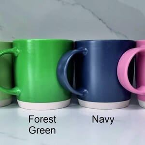 K&ouml;nnte beinhalten: Vier Keramikbecher in verschiedenen Farben: Mintgr&uuml;n, Waldgr&uuml;n, Marineblau und Pink. Jeder Becher hat einen wei&szlig;en Streifen am Boden.