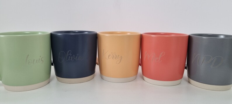 K&ouml;nnte beinhalten: F&uuml;nf Keramikbecher mit verschiedenen Glasuren und personalisierten Namen: Louis, Olivia, Kerry, Noel und NPO. Die Becher haben einen wei&szlig;en Rand und Boden.