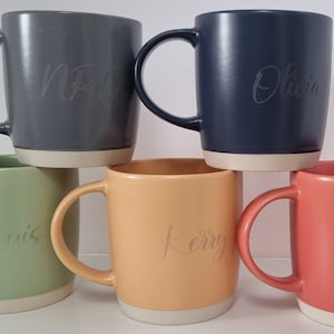 K&ouml;nnte beinhalten: F&uuml;nf Keramikbecher mit verschiedenen Glasuren. Die Becher sind pyramidenf&ouml;rmig gestapelt. Die Becher sind mit den Namen "Olivia", "Kerry", "Luis", "NP" und "Lori" personalisiert.