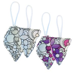 May include: Four decorative, teardrop-shaped fabric ornaments. Two are white with black floral and circular patterns, and two are white with purple and pink floral designs. Each ornament has a white cord loop for hanging.