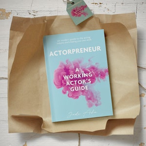 Puede incluir: Un libro titulado "Actorpreneur: A Working Actor's Guide" de Jade Aba. La portada del libro presenta un fondo azul con diseños rosados ​​en forma de humo.
