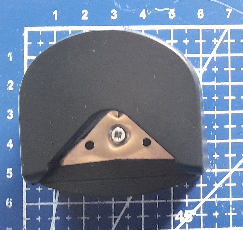 May include: A black and silver corner rounder tool with a triangular blade and a screw in the center. The tool is designed to round the corners of paper or cardstock.