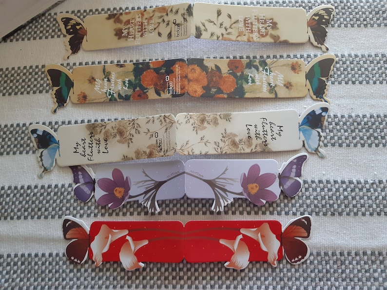May include: Set of six colorful bookmarks featuring butterflies and floral designs. Each bookmark has a different design and includes a quote about love. The bookmarks are made of sturdy cardstock and are perfect for marking your place in a book.