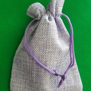 May include: A small, lavender-colored drawstring bag made of woven fabric. The bag has a purple drawstring and is closed.