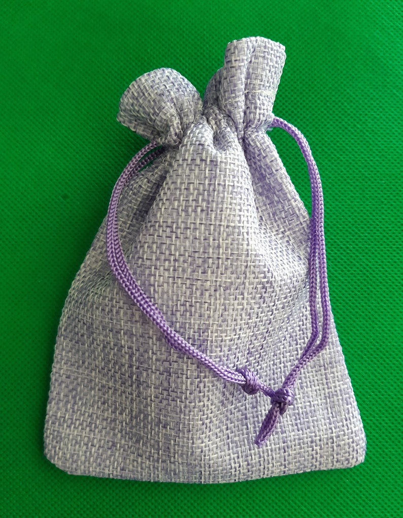May include: A small, lavender-colored drawstring bag made of woven fabric. The bag has a purple drawstring and is closed.