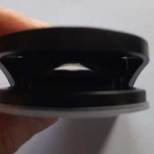 May include: A black and white phone grip with a circular design. The grip has a sticky base and a ring that can be used to hold the phone.