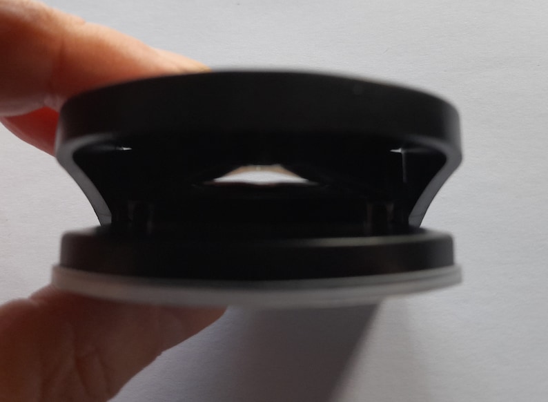May include: A black and white phone grip with a circular design. The grip has a sticky base and a ring that can be used to hold the phone.