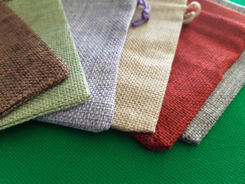 May include: Six small burlap pouches in various colors, including brown, green, purple, beige, red, and gray. The pouches are arranged in a stack, with the brown pouch on the bottom and the gray pouch on the top.