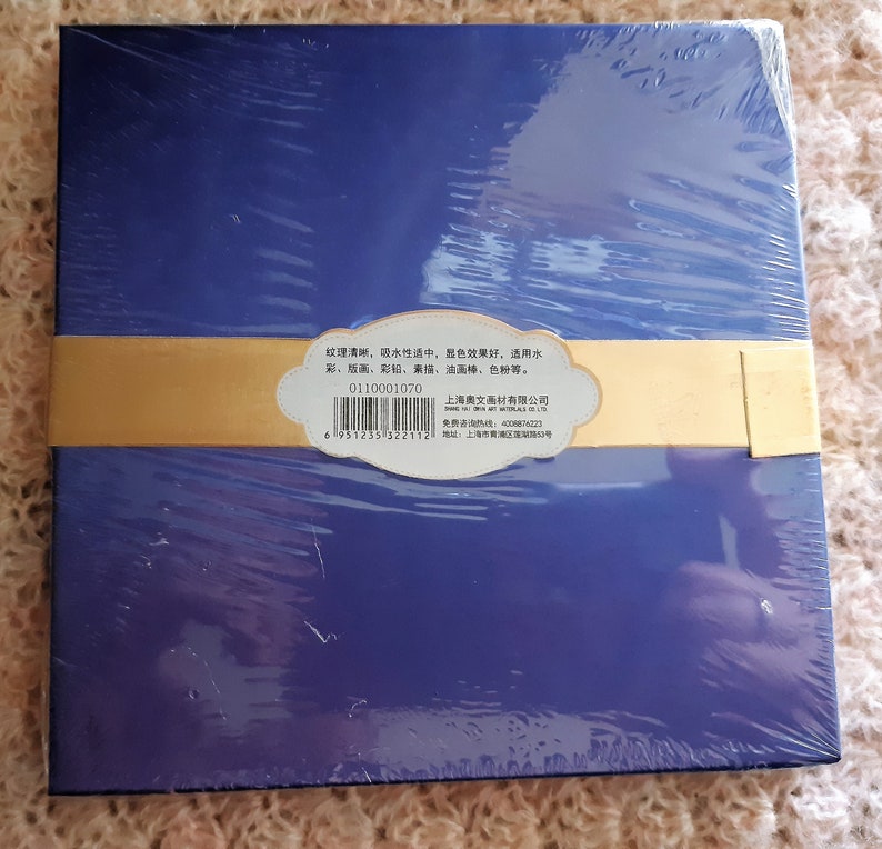 K&ouml;nnte beinhalten: Eine blaue Box mit einem goldenen Etikett. Das Etikett enth&auml;lt Text in Chinesisch und Englisch. Der Text auf dem Etikett lautet: "Die Textur ist klar, die Wasseraufnahme ist mittelm&auml;&szlig;ig, der Farbeffekt ist gut, geeignet f&uuml;r Aquarell, Gouache, Buntstift, Skizzieren, &Ouml;lpastell, Farbpulver usw. Shanghai Aowen Art Materials Co., Ltd. Kostenlose Hotline: 4008876223 Adresse: Shanghai City"