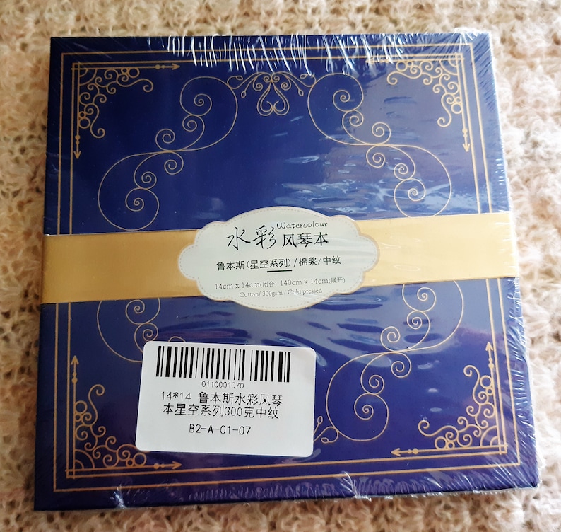 K&ouml;nnte beinhalten: Ein blaues Aquarell-Skizzenbuch mit goldenen Akzenten und dem Text "Watercolour 水彩风琴本 鲁本斯(星空系列)/棉浆/中紋 14cm x 14cm(合)140cmx14cm(展开) Cotton/300gsm/Cold pressed 0110001070 14*14 鲁本斯水彩风琴本星空系列300克中纹 B2-A-01-07" auf dem Einband.