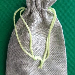 May include: A small, light gray drawstring bag made of burlap with a light green drawstring.