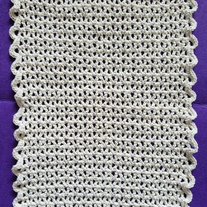 May include: A rectangular, off-white crochet piece with a scalloped edge. The open weave design creates a textured appearance. This handmade item could be a washcloth, doily, or part of a larger craft project.