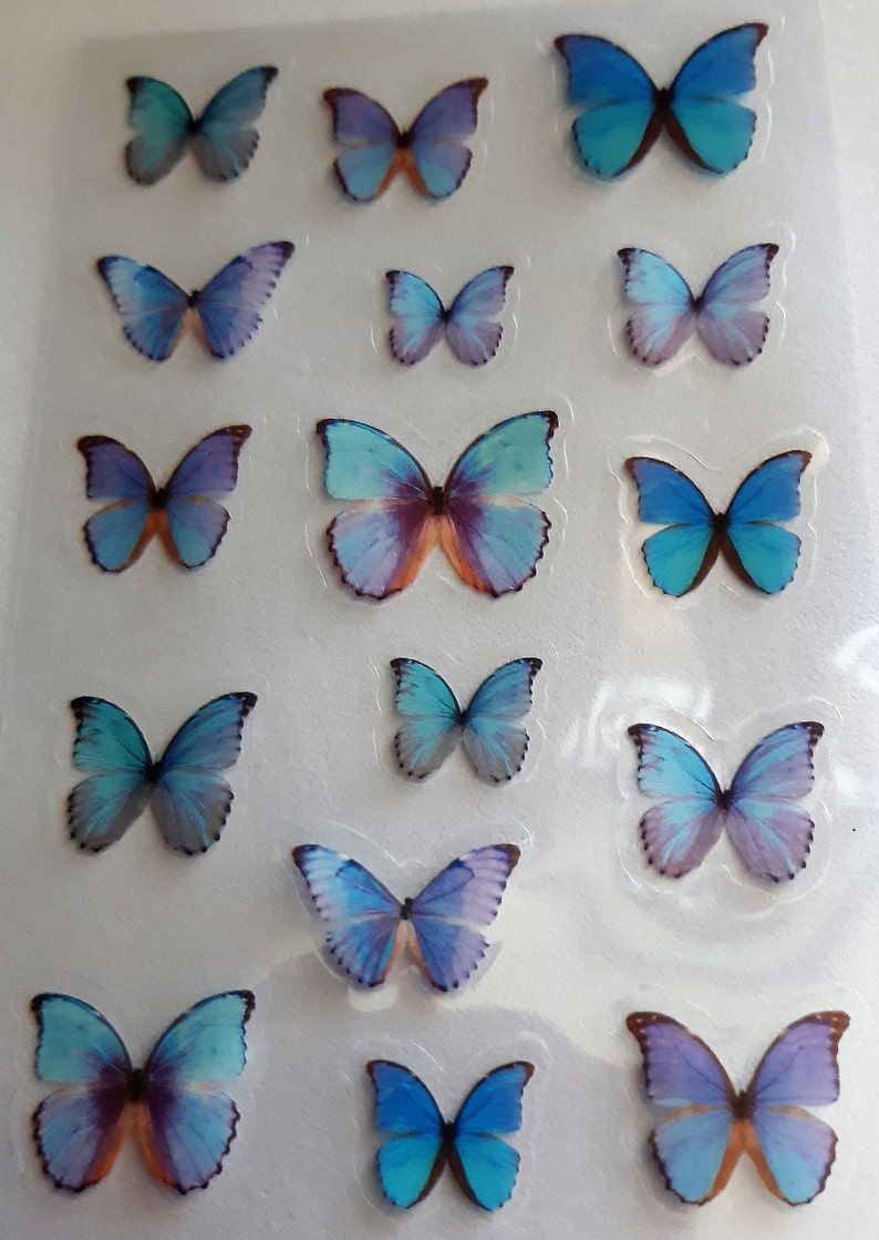 Może przedstawiać: Arkusz naklejek z niebieskimi i fioletowymi motylami. Motyle są ułożone w rzędach na przezroczystej folii plastikowej.