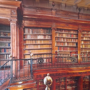 Könnte beinhalten: Eine große, hölzerne Bibliothek mit mehreren Ebenen von Bücherregalen, die mit Büchern gefüllt sind. Die Regale sind aus dunklem Holz und haben aufwendige Schnitzereien. Die Bibliothek hat einen Balkon mit einem schmiedeeisernen Geländer.