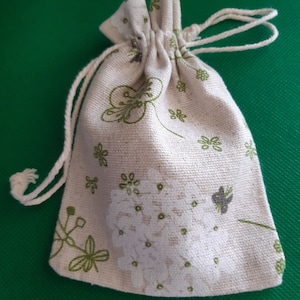 May include: A small, white drawstring bag with a floral pattern. The bag is made of a natural fabric and has a white drawstring closure.