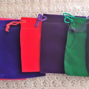 Puede incluir: Siete bolsitas de terciopelo con cordón de ajuste en varios colores, incluyendo burdeos, rosa, morado, rojo, morado oscuro, verde y negro.
