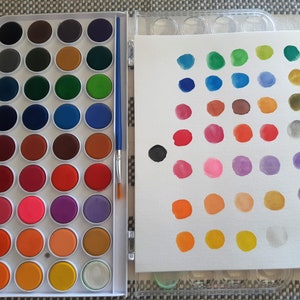 May include: A white plastic watercolor paint set with a variety of colors in round pans. The set includes a brush and a white canvas for painting.