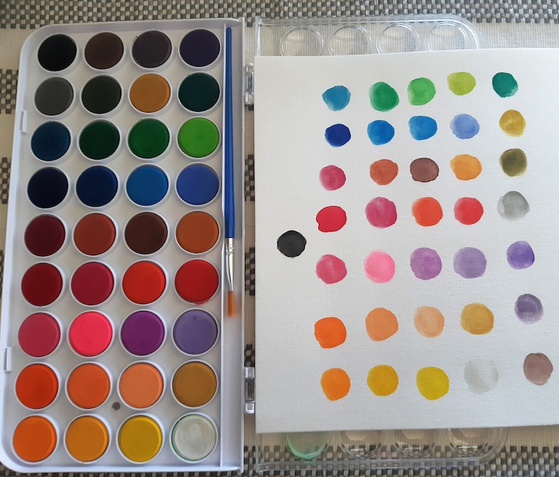May include: A white plastic watercolor paint set with a variety of colors in round pans. The set includes a brush and a white canvas for painting.