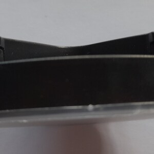 May include: A black plastic base with a clear plastic top. The base has a slightly curved shape.