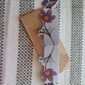 May include: Two purple and white butterfly bookmarks with a flower design. The bookmarks are on a brown envelope with the text "HOLO" and "281.700.0038" printed on it.