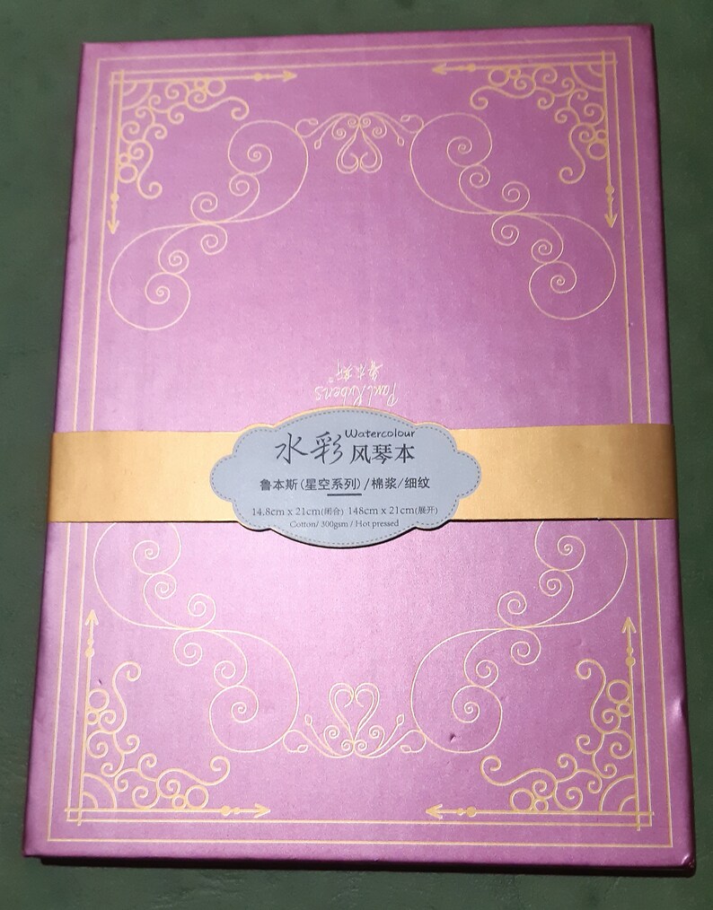 K&ouml;nnte beinhalten: Ein violetter Aquarell-Skizzenblock mit goldener Dekorrand und dem Text "Watercolour 水彩风琴本" auf der Vorderseite. Der Text unter dem Titel lautet "鲁本斯(星空系列)/棉浆/细纹 14.8cm x 21cm(所) 148cm x 21cm(展开) Cotton/300gsm/Hot pressed".