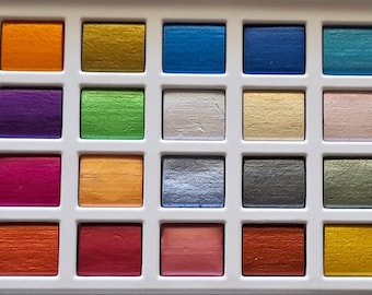 May include: A set of 36 watercolor paints in a white plastic tray. The paints are arranged in a grid pattern and include a variety of colors, including gold, silver, red, blue, green, and purple.