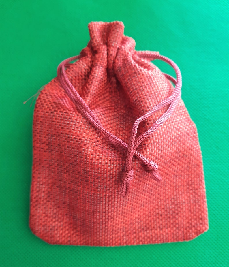 May include: A red drawstring bag made of burlap fabric. The bag is closed with a knotted cord.