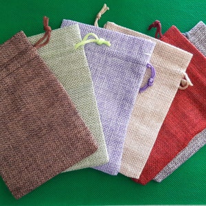 May include: Six small burlap drawstring bags in various colors, including brown, green, purple, beige, red, and gray. The bags are arranged in a semi-circle on a green surface.