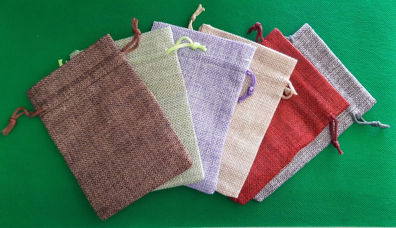 May include: Six small burlap drawstring bags in various colors, including brown, green, purple, beige, red, and gray. The bags are arranged in a semi-circle on a green surface.