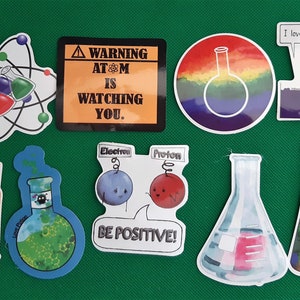 Può includere: Una collezione di adesivi a tema scientifico con vari disegni, tra cui un atome, becher e un cartello di avvertimento che recita "ATTENZIONE ATM TI STA OSSERVANDO."