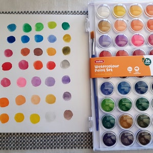 May include: A set of 36 watercolor paints in a plastic case with a brush. The paints are arranged in a grid pattern and include a variety of colors, including red, blue, green, yellow, and brown. The case is labeled "Watercolour Paint Set" and includes 36 colors.