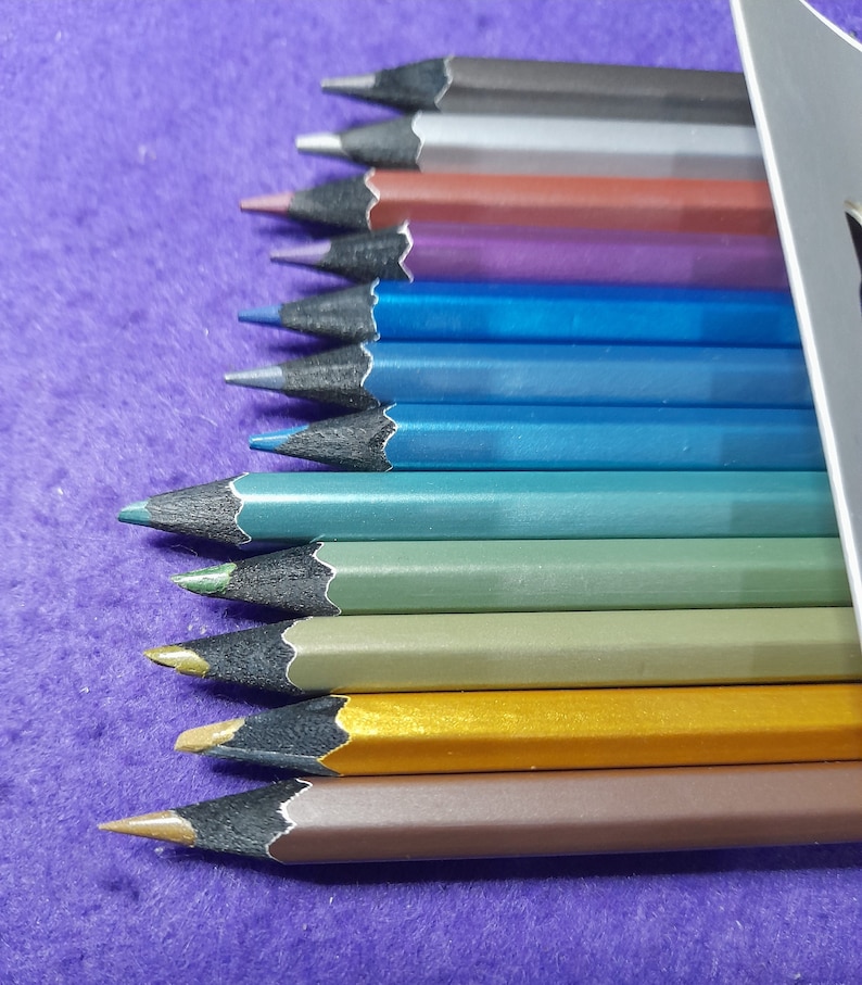Pu&ograve; includere: Un set di 12 matite colorate metallizzate con involucri in legno nero. Le matite sono disposte in fila, con le punte rivolte verso lo spettatore. I colori sono: argento, grigio, marrone, viola, blu, blu verde, verde, oro e bronzo.